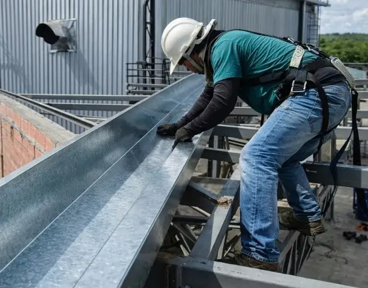 Profissional manuseando calha metálica em telhado de estrutura industrial